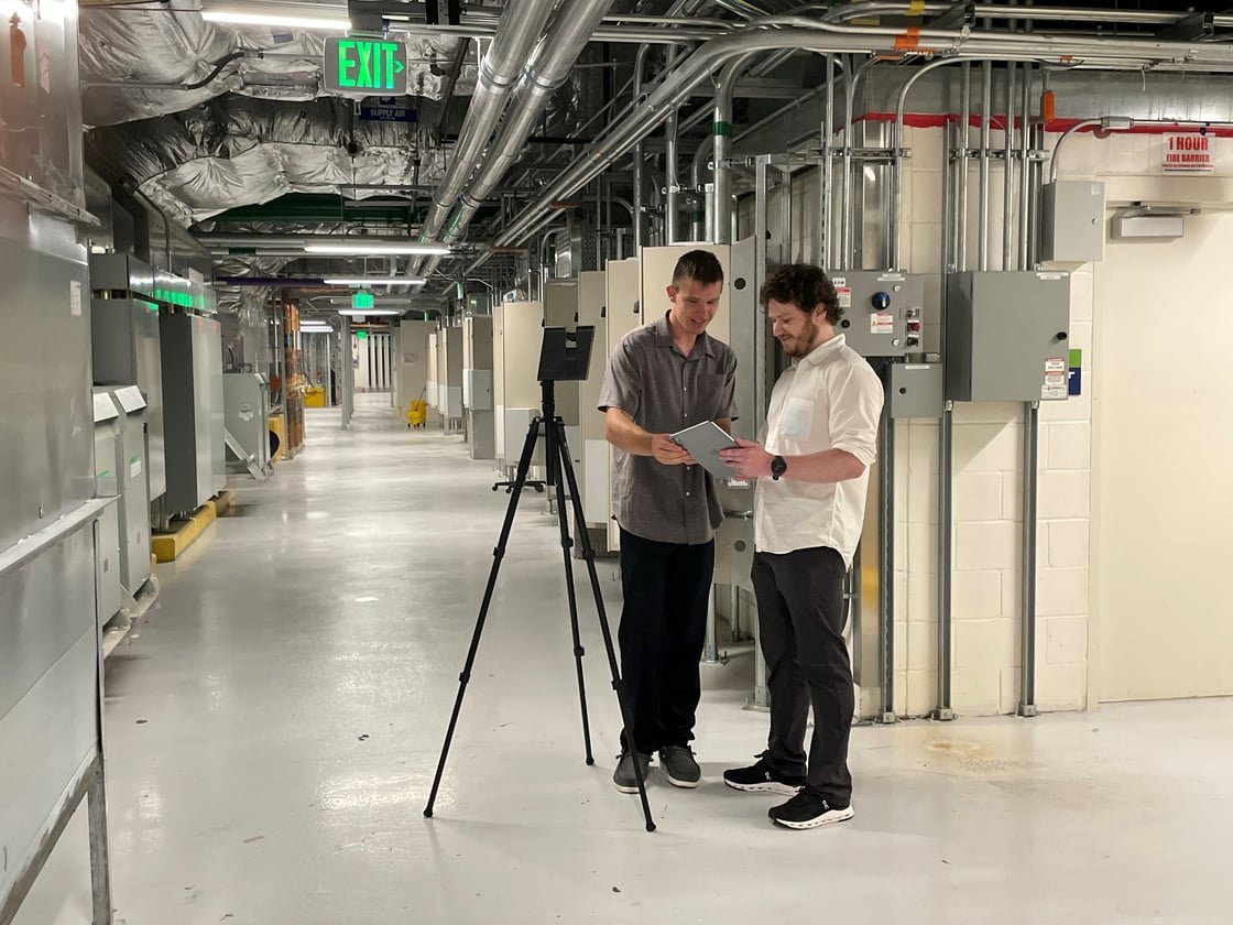 SMS technicians reviewing a tablet beside the capture camera in a facility corridor